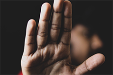 A person's face emerges from a dark background, their hand held up in front of the camera as a clear gesture of "No" or "Stop.”