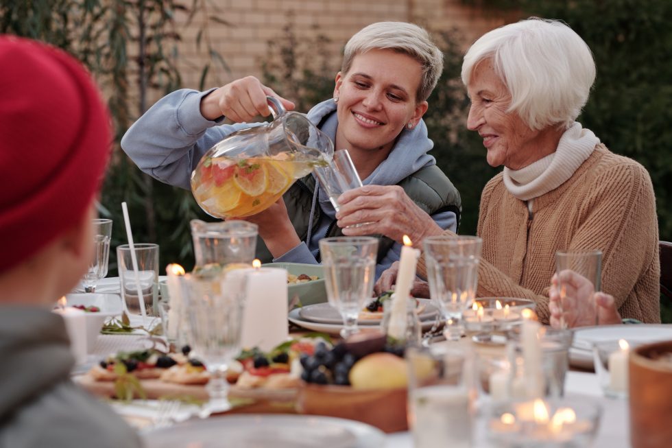 A younger woman pours a glass of juice for a senior woman.