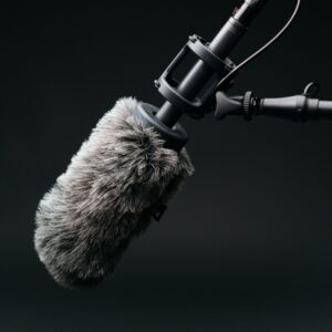A gray studio microphone is angled downwards with a black backdrop.
