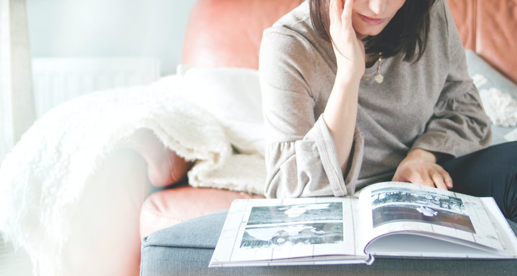 A woman sitting down, poring over a book filled with photographs.