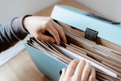 A person’s hands flip through an accordion file folder, searching for something.