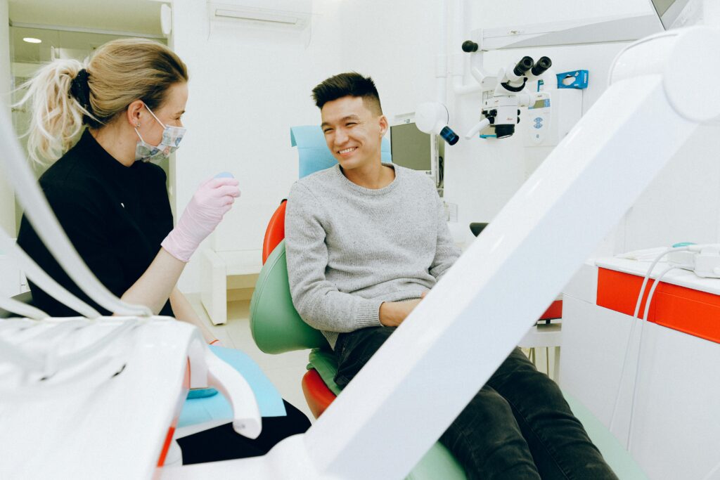 Man sits on chair at dentist's office as dentist gets ready to examine him.