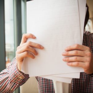  Person holding a stack of papers in front of their face with both hands.