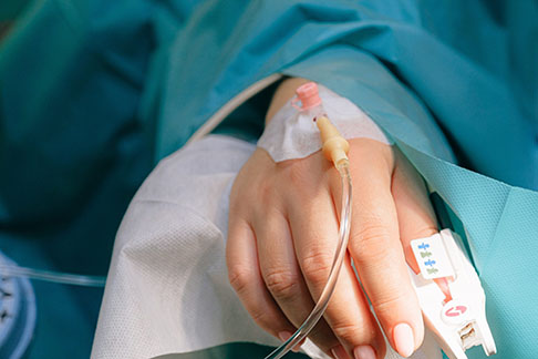 A hand with IV tubing attached, On a hospital bed. 